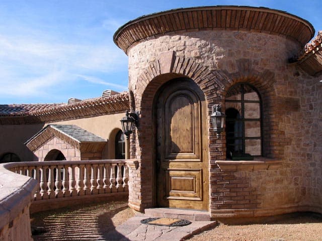 Curved stone entry tower with an arched wood door and balcony