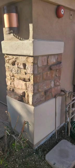 Column clad in tan and rust brick-shaped stone with a cast stone cap and light fixture above