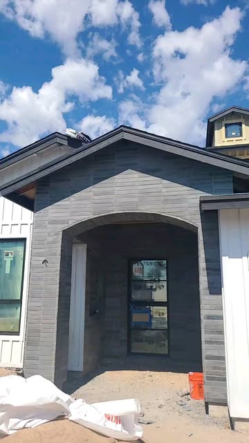 Gabled entry porch clad in dark grey linear stone with an arched opening, under construction