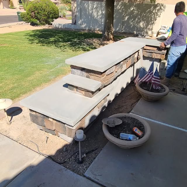 Outdoor stone bar and seating wall with poured concrete countertops being finished in a front yard