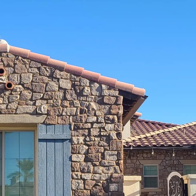 Tan and rust fieldstone gable end and column on a tile-roofed home against a clear blue sky