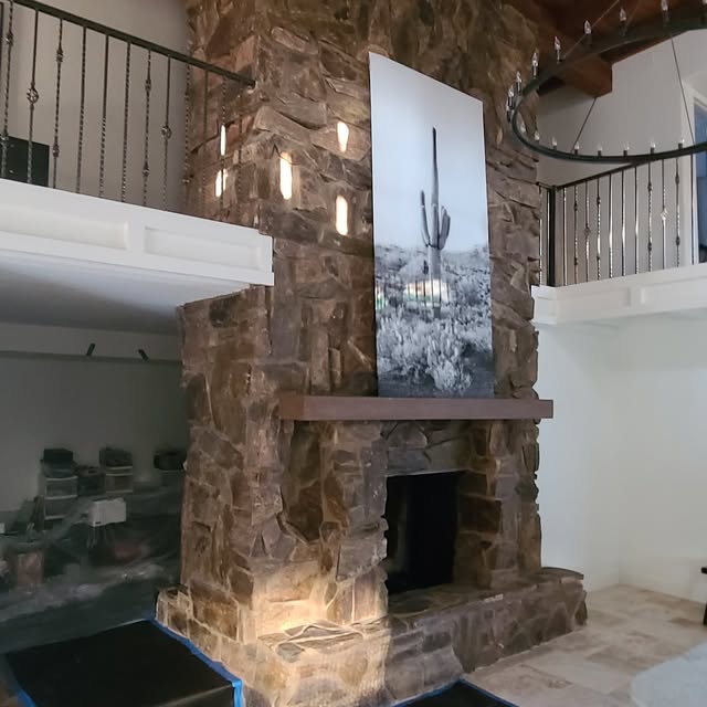 Two-story interior fireplace faced in brown fieldstone with a timber mantel and wrought iron stair railings